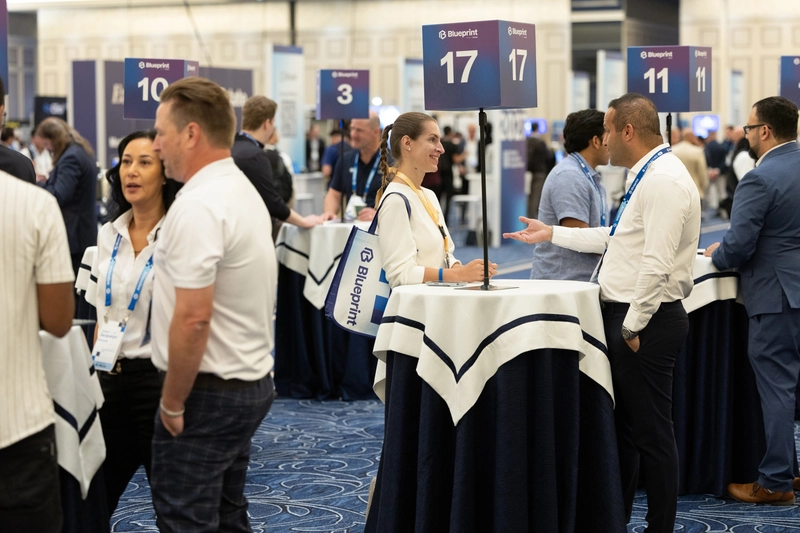 Business professionals networking at career fair with numbered booth signs and branded tote bags